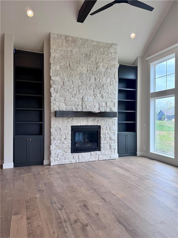 7719 NE 103rd Ter, Kansas City, MO 64157 - unfurnished living room with ceiling fan, plenty of natural light, wood finished floors, vaulted ceiling, and a stone fireplace