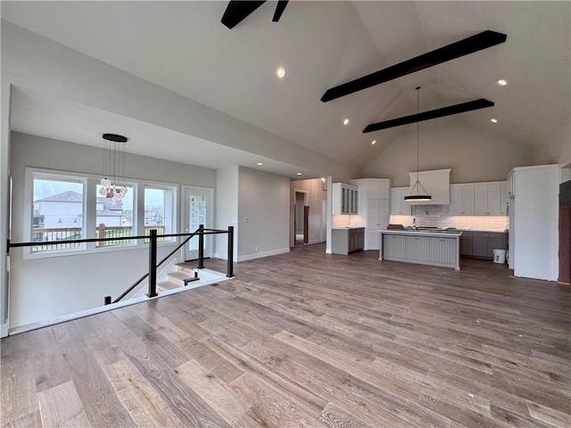 7719 NE 103rd Ter, Kansas City, MO 64157 - unfurnished living room featuring beam ceiling, high vaulted ceiling, wood finished floors, ceiling fan, and a chandelier