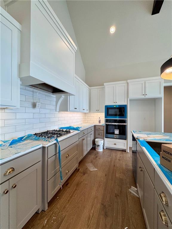 7719 NE 103rd Ter, Kansas City, MO 64157 - kitchen featuring stainless steel oven, premium range hood, dark wood-style flooring, backsplash, and vaulted ceiling