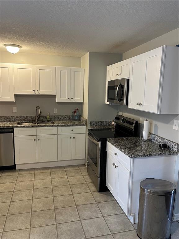 kitchen featuring appliances with stainless steel finishes, a textured ceiling, sink, light tile patterned floors, and white cabinetry