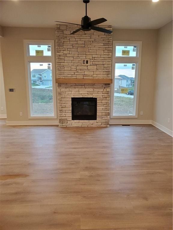 unfurnished living room with ceiling fan, a healthy amount of sunlight, a stone fireplace, and light wood-type flooring