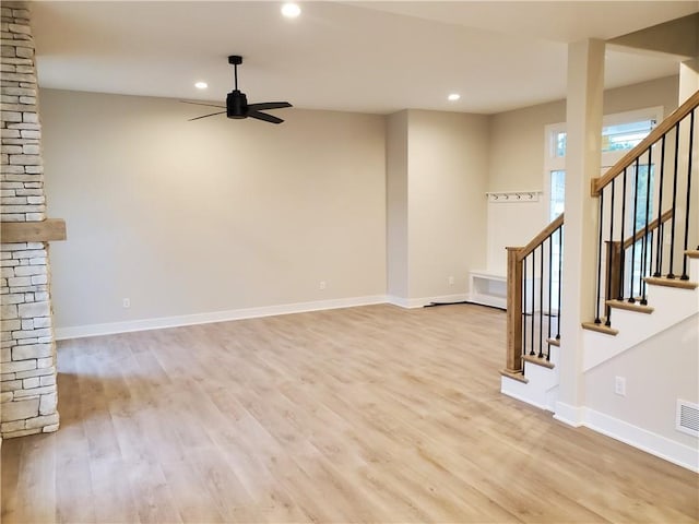 unfurnished living room featuring ceiling fan, a stone fireplace, and light wood-type flooring