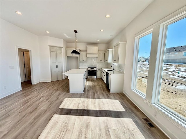 kitchen featuring a sink, a kitchen island, hanging light fixtures, light countertops, and stainless steel range