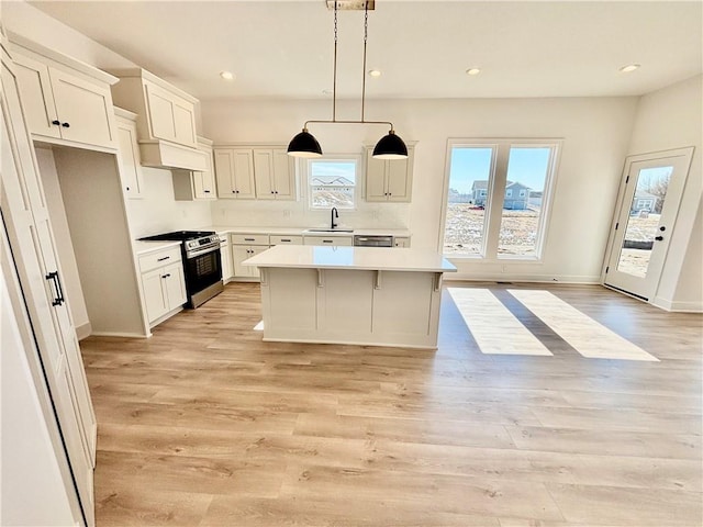 kitchen featuring a kitchen island, appliances with stainless steel finishes, light countertops, white cabinetry, and pendant lighting