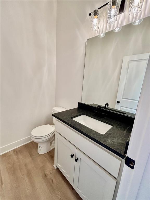 half bathroom featuring toilet, baseboards, wood finished floors, and vanity