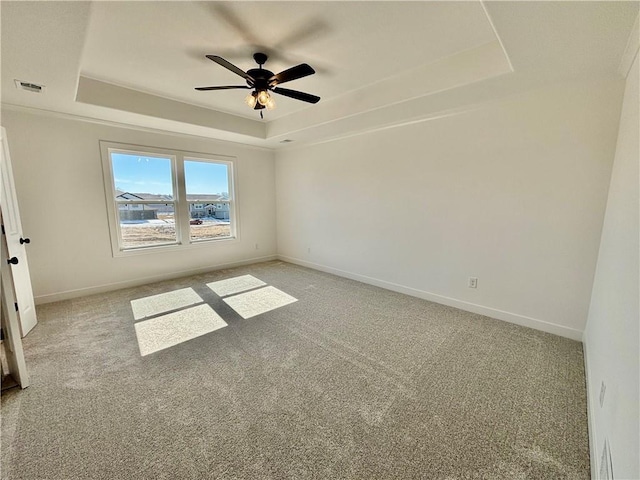 spare room featuring visible vents, baseboards, a ceiling fan, light colored carpet, and a tray ceiling