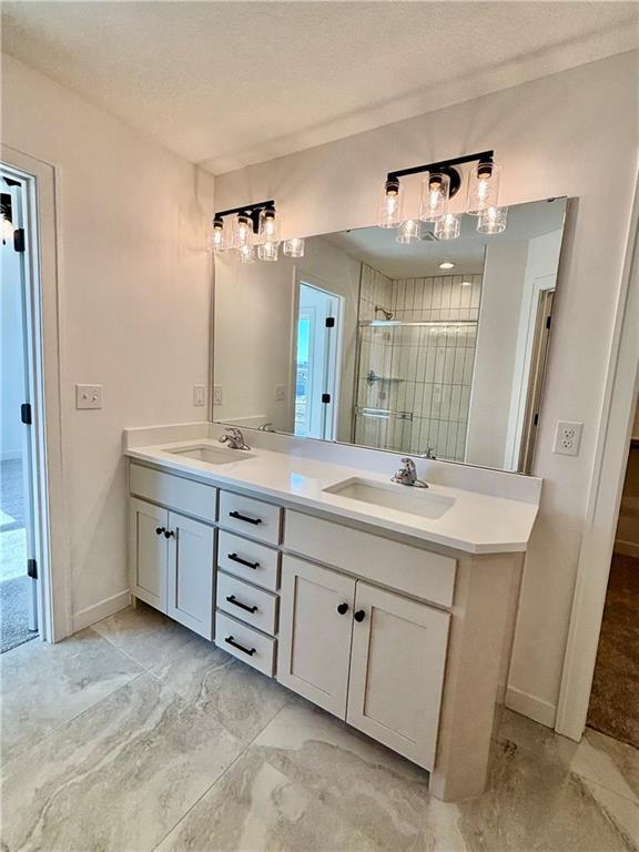 full bathroom with a sink, a shower stall, a textured ceiling, and double vanity