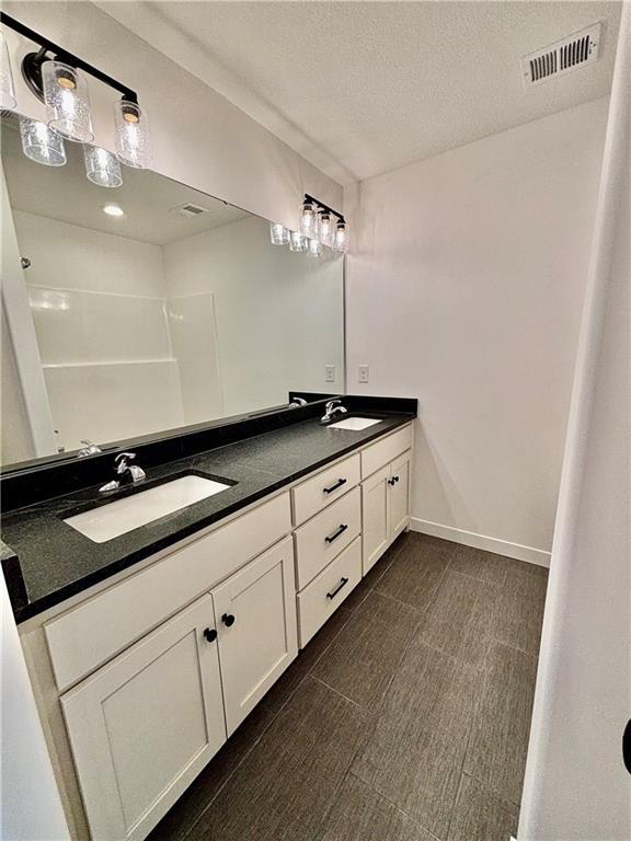 full bath featuring double vanity, visible vents, a sink, a textured ceiling, and baseboards