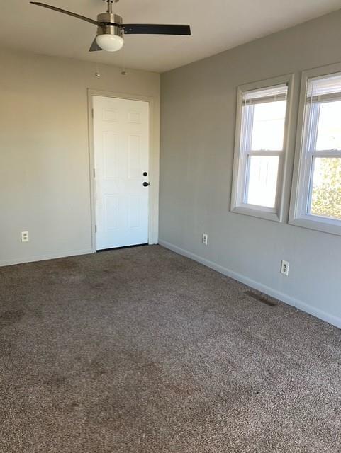 spare room featuring dark colored carpet and ceiling fan