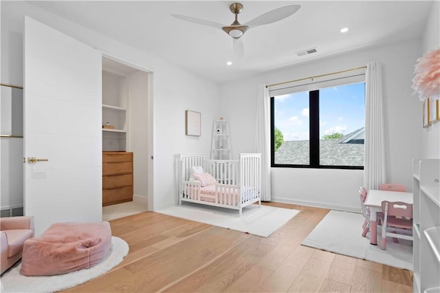 bedroom featuring ceiling fan, wood-type flooring, and a crib