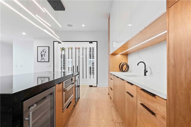 kitchen with light brown cabinetry, beverage cooler, sink, light hardwood / wood-style flooring, and white cabinetry