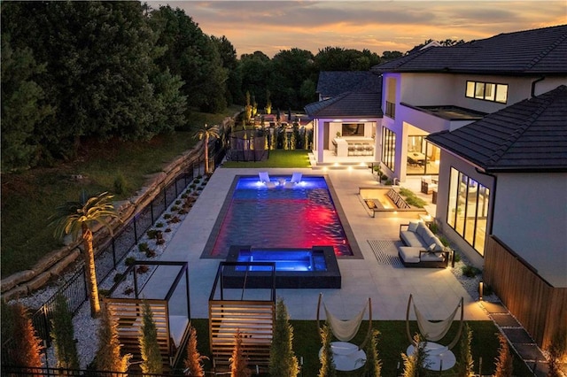 pool at dusk with an in ground hot tub, pool water feature, and a patio area