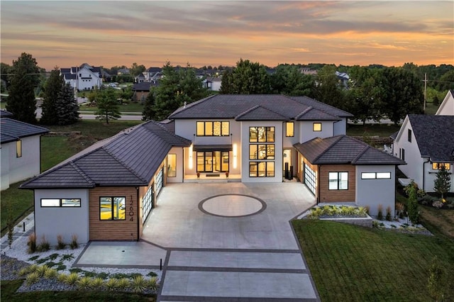 12604 W 160th St, Overland Park, KS 66062 - back of property at dusk with curved driveway, a garage, a yard, stucco siding, and a tile roof