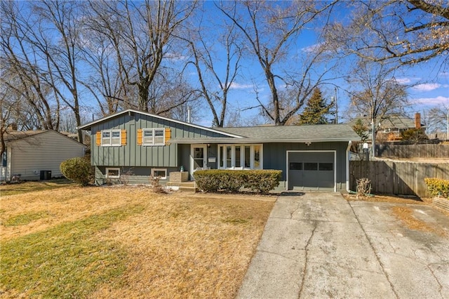 tri-level home featuring driveway, fence, board and batten siding, a front yard, and a garage