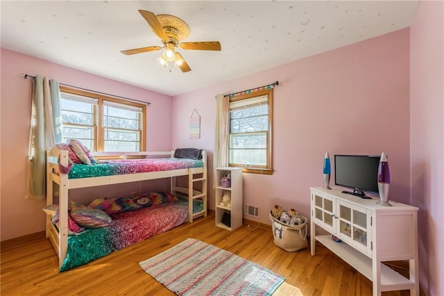 bedroom featuring multiple windows, wood finished floors, visible vents, and ceiling fan