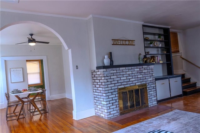 living room featuring hardwood / wood-style flooring, built in shelves, ceiling fan, ornamental molding, and a fireplace