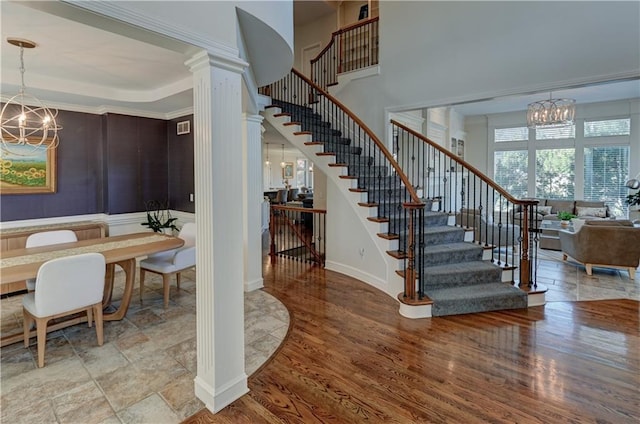 staircase with ornate columns, crown molding, and an inviting chandelier