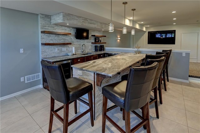 bar with light stone countertops, decorative backsplash, sink, pendant lighting, and light tile patterned flooring