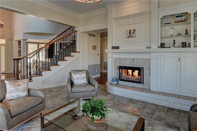 living room with a chandelier, decorative columns, a tile fireplace, and ornamental molding