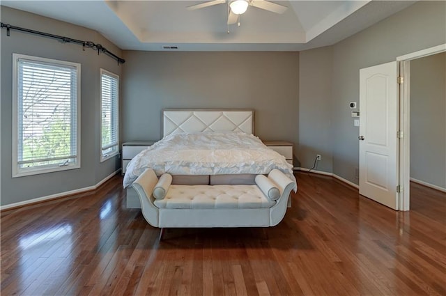 bedroom with ceiling fan, dark hardwood / wood-style flooring, and a tray ceiling