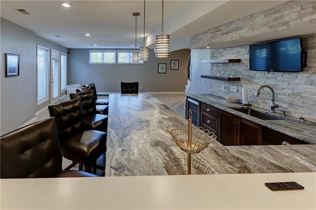 kitchen with sink, wine cooler, light stone counters, decorative light fixtures, and decorative backsplash