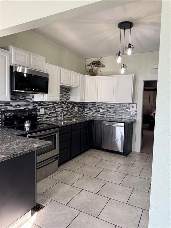 kitchen featuring dark stone counters, white cabinets, decorative backsplash, decorative light fixtures, and stainless steel appliances