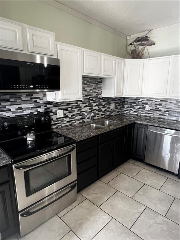 kitchen with appliances with stainless steel finishes, backsplash, dark stone counters, sink, and white cabinetry