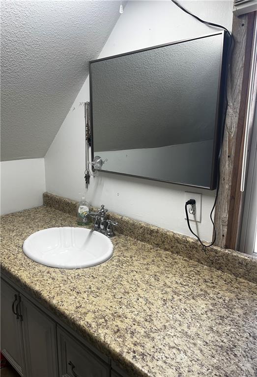 bathroom with a textured ceiling, vanity, and vaulted ceiling