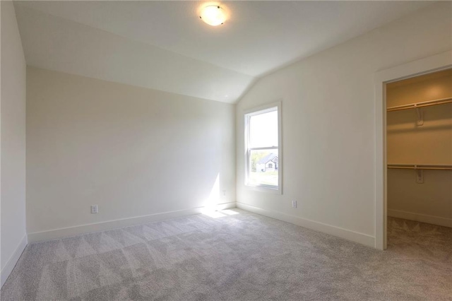 unfurnished bedroom with vaulted ceiling, light colored carpet, a spacious closet, and a closet