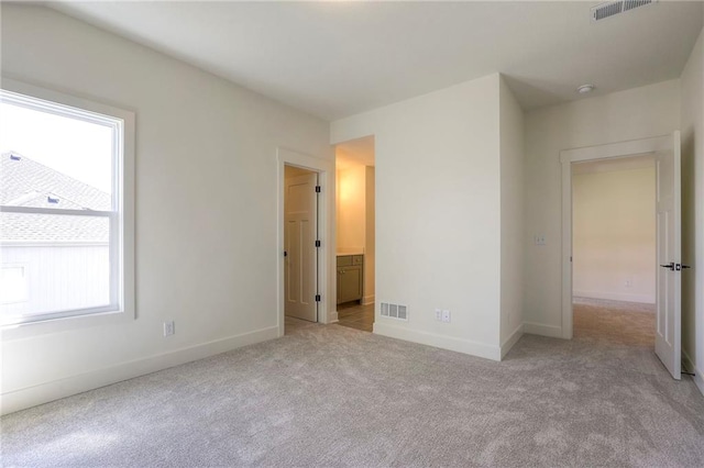 unfurnished bedroom featuring multiple windows, light carpet, and ensuite bathroom