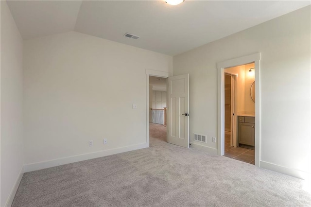 unfurnished bedroom featuring vaulted ceiling, light colored carpet, and ensuite bath