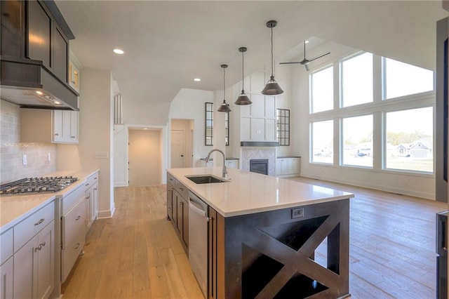 kitchen featuring sink, backsplash, an island with sink, stainless steel gas stovetop, and light wood-type flooring