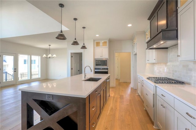 kitchen featuring sink, decorative light fixtures, a kitchen island with sink, white cabinets, and light wood-type flooring