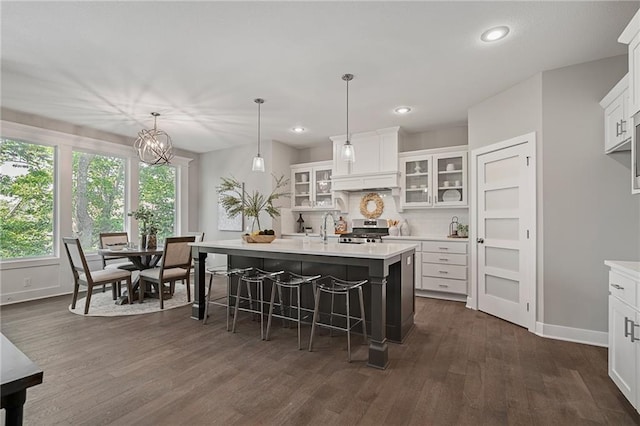 kitchen with pendant lighting, a kitchen island with sink, white cabinets, stainless steel range, and dark hardwood / wood-style flooring