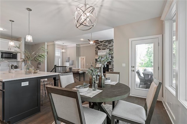 dining area featuring dark hardwood / wood-style floors, a large fireplace, sink, and ceiling fan with notable chandelier