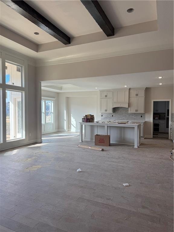 unfurnished living room featuring a tray ceiling, beamed ceiling, and light wood finished floors