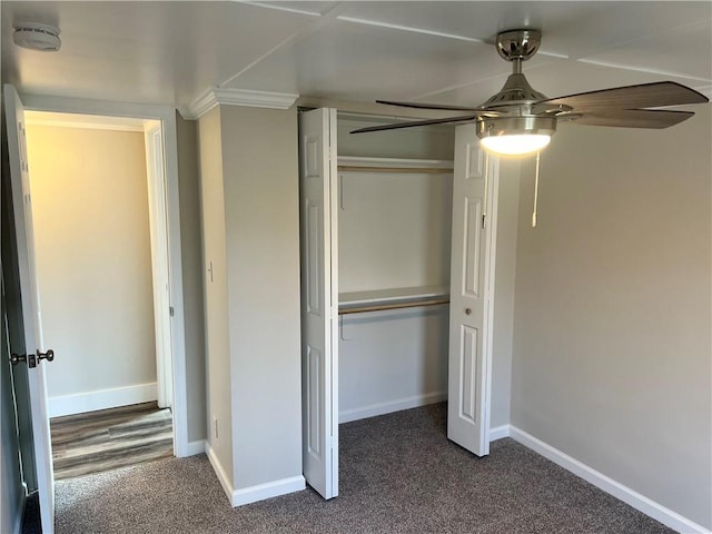 unfurnished bedroom featuring dark colored carpet, a closet, ceiling fan, and crown molding