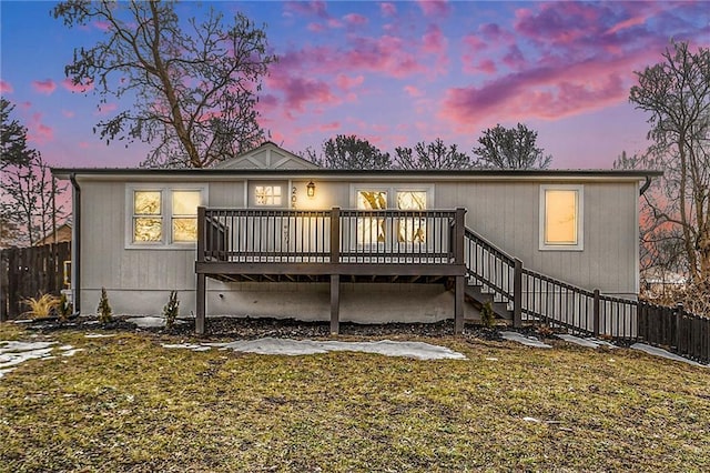 back house at dusk with a deck and a lawn