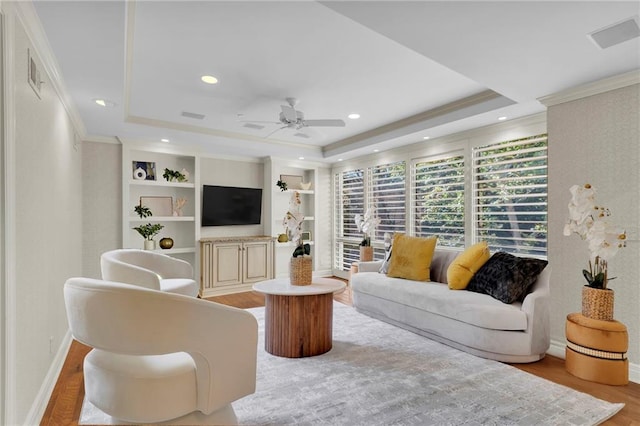 living room featuring a tray ceiling, light hardwood / wood-style flooring, ceiling fan, and ornamental molding