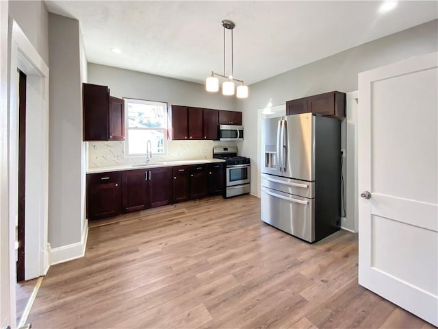 kitchen with pendant lighting, sink, decorative backsplash, light wood-type flooring, and stainless steel appliances