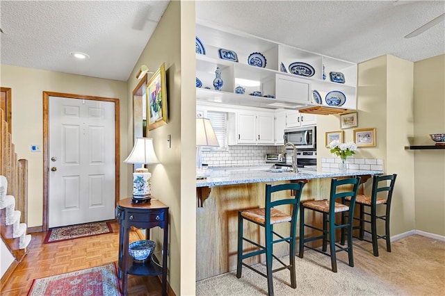 kitchen featuring stainless steel appliances, light stone counters, light parquet floors, a breakfast bar, and white cabinets