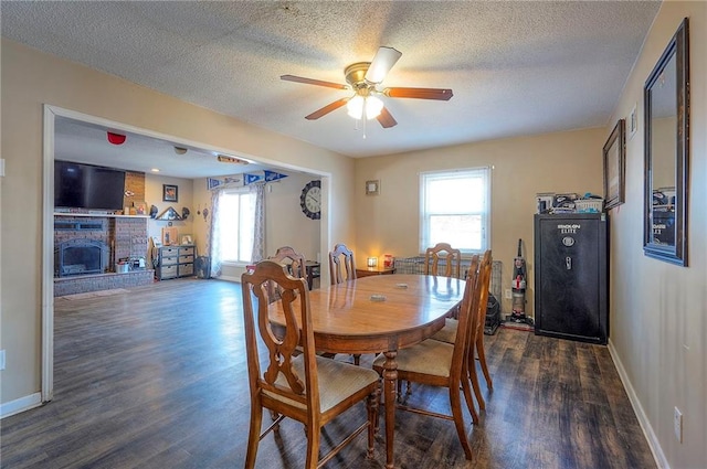 dining area featuring a ceiling fan, wood finished floors, baseboards, a textured ceiling, and a brick fireplace