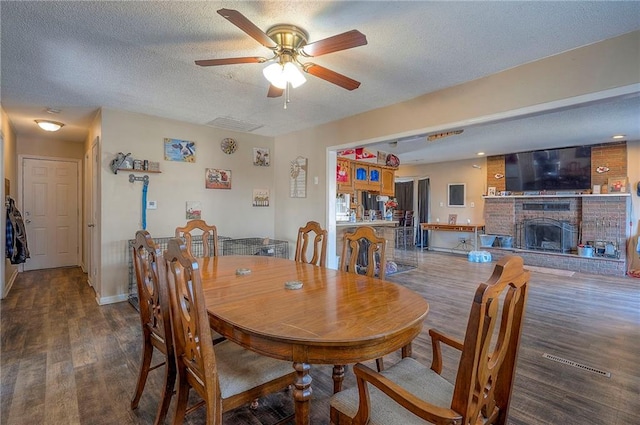 dining room with a brick fireplace, a textured ceiling, ceiling fan, and wood finished floors