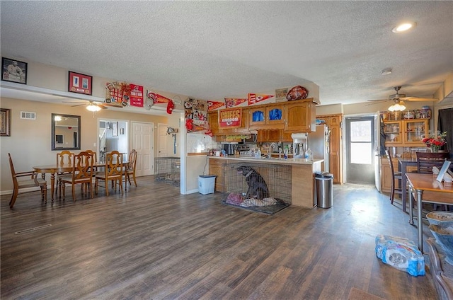 kitchen with brown cabinetry, a ceiling fan, visible vents, dark wood-type flooring, and light countertops