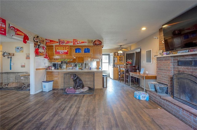 kitchen with a textured ceiling, a brick fireplace, wood finished floors, and a ceiling fan