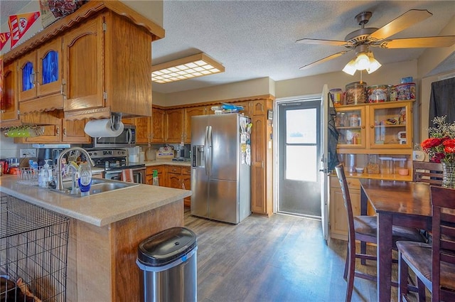 kitchen with ceiling fan, light wood-type flooring, appliances with stainless steel finishes, a peninsula, and brown cabinetry