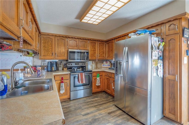 kitchen featuring dark wood finished floors, light countertops, brown cabinetry, stainless steel appliances, and a sink