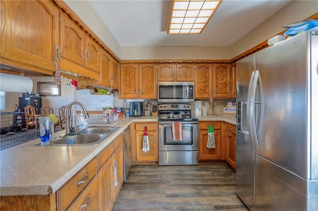 kitchen with brown cabinets, a sink, dark wood finished floors, appliances with stainless steel finishes, and light countertops