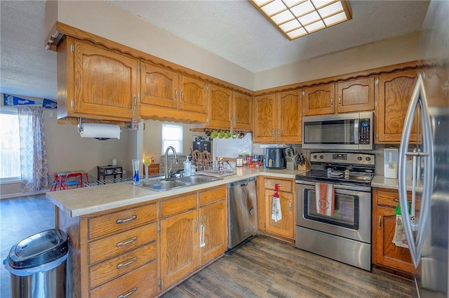 kitchen featuring brown cabinetry, dark wood-style flooring, a sink, light countertops, and appliances with stainless steel finishes