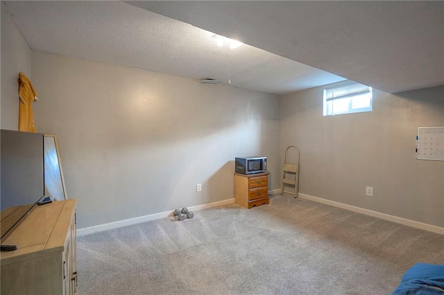 basement featuring light colored carpet, a textured ceiling, and baseboards